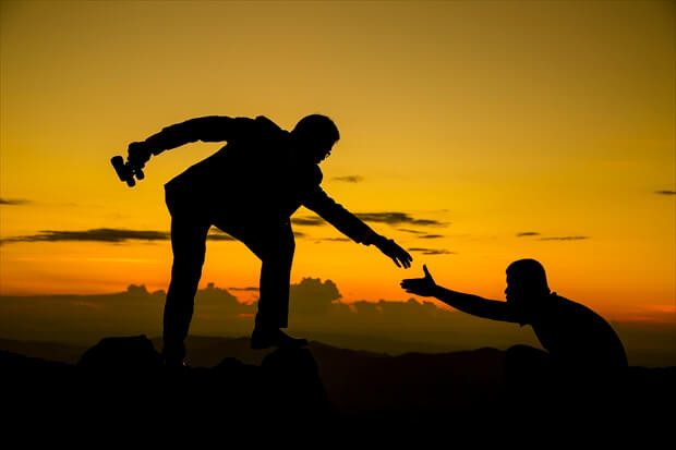 Businessman gived hand for pull team to peak of  mountain for work together.